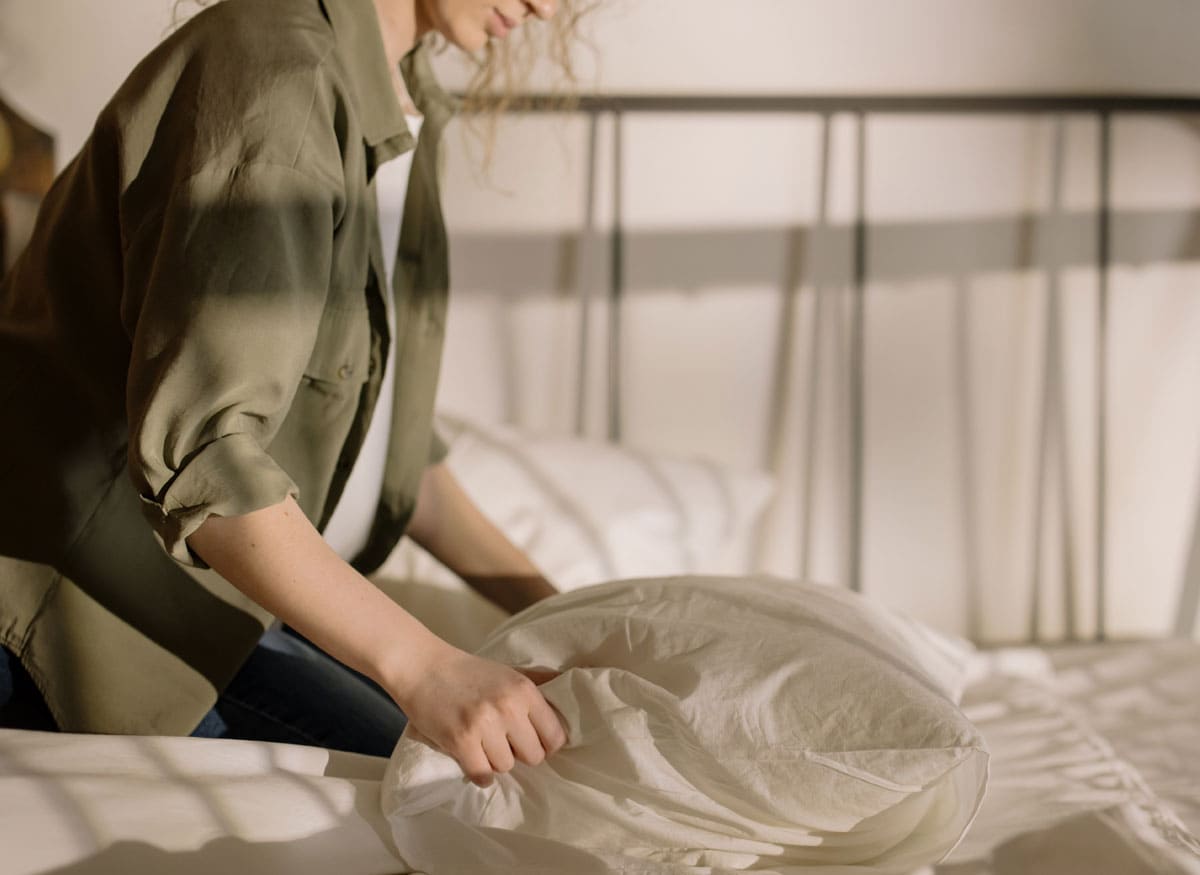Una mujer hace una cama en una habitación tenuemente iluminada. Cuidamos de ti, servicios sociales